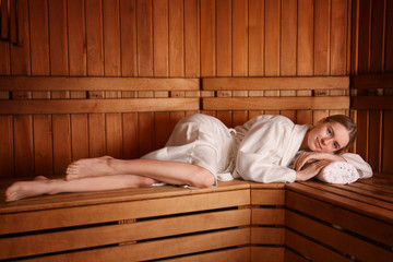 Young woman lying on wooden bench in sauna