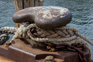Fototapeta na wymiar Ropes and chains tied to moorings on rusty weathered mooring bollard on dock