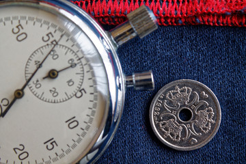 Denmark coin with a denomination of one crown (krone) (back side) and stopwatch on dark blue denim with red stripe backdrop - business background