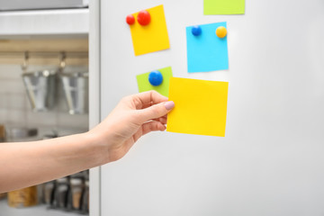 Woman holding empty note near refrigerator door in kitchen