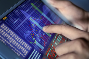 Broker using tablet computer with stock data on screen, closeup