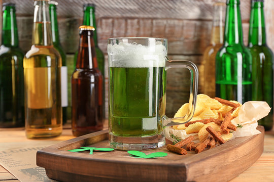 Glass of green beer and snacks on wooden board. Saint Patrick's day celebration