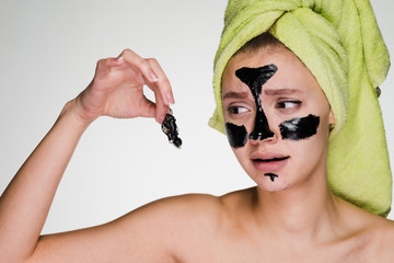 sad young girl with a green towel on her head removes a black mask from her face, it hurts