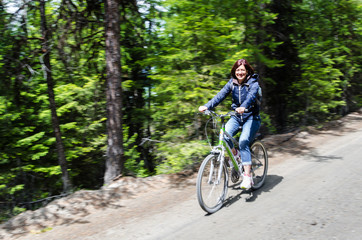 Fototapeta na wymiar Smiling Woman Riding a Bicycle on an Unpaved Road through a Forest on a Sunny Spring Day. Blurred Motion.