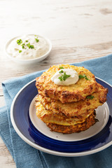 golden fried rosti pile from cauliflower and parmesan cheese with a creamy dip and parsley garnish, blue napkin, bright wooden table with copy space, vertical