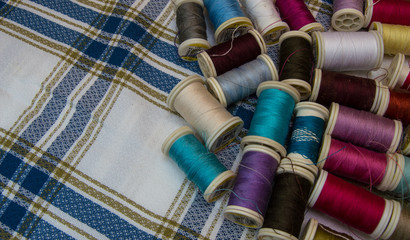 A lot of yarn spools of many colors on pretty checkered fabric. Tailoring material for sewing with space with nothing.