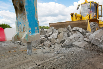 Fototapeta premium Large jackhammer crushing asphalt paving during road construction works and wheel loader moving break stones in bucket