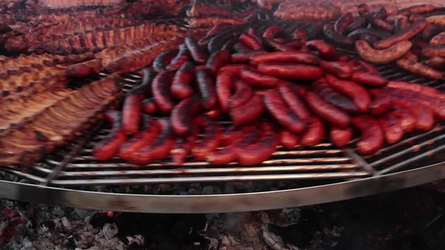 Parrilla girando con carnes asadas al aire libre. Carnes de cerdo, chorizos, salchichas y longanizas