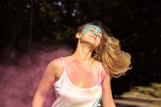 Cool blonde woman with long curly hair fluttering on wind with Holi dry paint