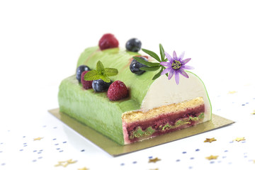 Pistachio Raspberry Yule Log decorated with fresh raspberries, blueberry, and pasion flower on white background.