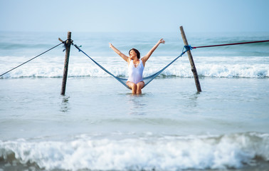 Pretty woman enjoy with ocean breeze and sun sits in hammock swing over the waves