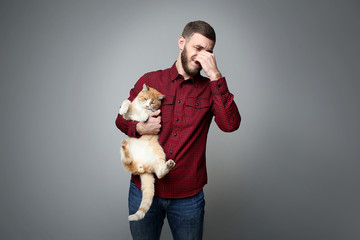 Young man with allergy holding cat on grey background