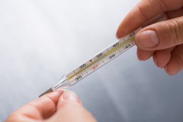 Hands holding mercury thermometer which shows febrile temperature on gray background