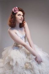Wedding Concepts. Cute and Sensual Caucasian Red-Haired Female in Tailored Wedding Dress. Posing With Hands on Petticoat Below. Against Gray Background.