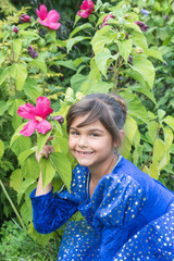 Portrait of smiling little girl in blue clothes holding a blooming hibiscus