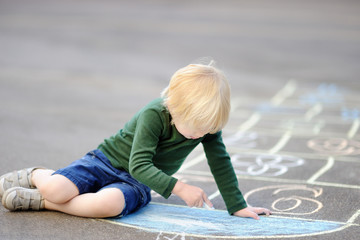 Cute little boy drawing hopscotch using chalk on asphalt