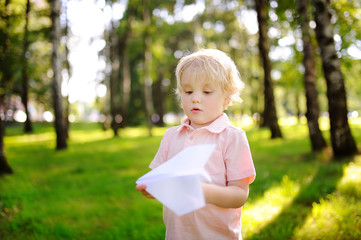 Cute toddler boy playing with paper plane in a summer park