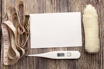 white sticky note with empty space for a text on wooden background. Health concept with thermometer bandage and metre