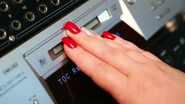 A female hand inserts a mini disc into a silvery player. The camera shoots static, close-up.