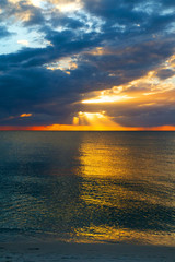Obraz na płótnie Canvas Amazing epic seascape of colorful sunset view from sandy beach, bright sunbeam rays of warm sun light transect the dark cloudy sky above blue sea