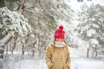 Fototapeta na wymiar Beautiful little girl have fun in snowy winter forest. Adorable child wearing a red knitted hat and jacket walk outdoor at Christmas. Kid playing in snowy forest. Family winter vacation in mountains