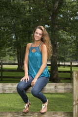 Obraz premium Beautiful teen girl poses while sitting on a wooden fence on farm in jeans and blouse
