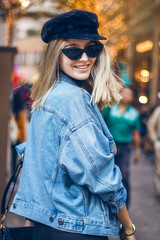 Portrait of a beautiful young blond woman with fashionable black sunglasses walking through street in Hong Kong. She is dressed in black clothes with a denim jacket and dancing on the street.