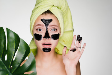 a surprised young girl with a green towel on her head applied a black mask to the problem areas on...