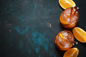 Summer alcoholic cocktail with bitter, sparkling wine, soda, orange and ice, dark background, top view