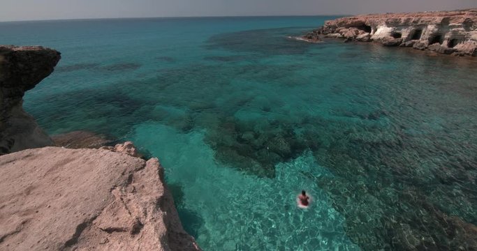 Young man jumping off cliff and diving into the sea