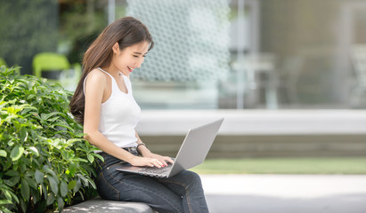 Beautiful young Asian freelance business woman working on her laptop while sitting outdoor in the city park