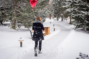woman walking in the woods on a snowy day holding red heart shaped balloon