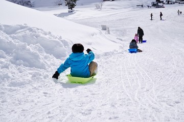 Fototapeta na wymiar スキー場でそり遊びをする子供