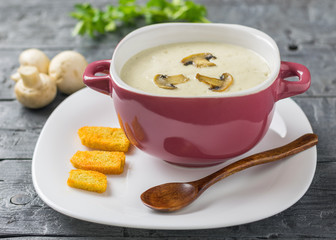 Freshly prepared cream soup of mushrooms with croutons on a white plate with a dark wooden spoon.