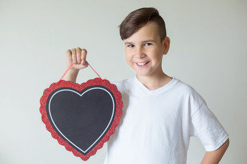 The boy holds a chalkboard in the form of a heart in his hands. Free space for your text. Beautiful...