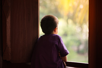 Little boy standing alone looking out of the window - 188320634