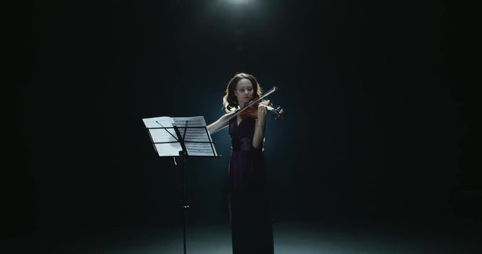 a talented girl violinist performs at her first solo concert, stage light, dark background