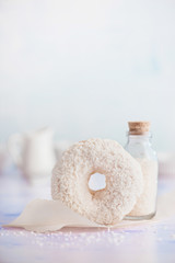 Coconut cream filled white donut with coconut topping on a light background. High key food photography. Bottle of coconut chips