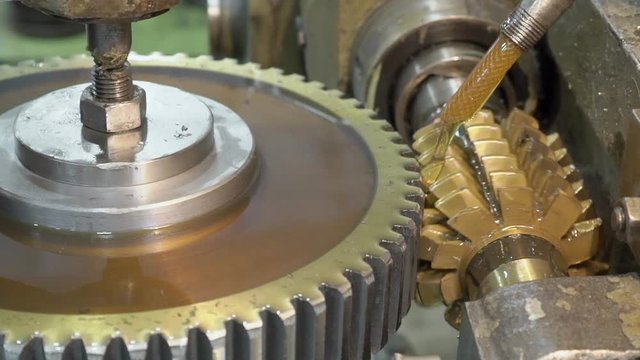 Close-up mechanism makes vertical grooves in pinion with oil. Jet of cooling yellow liquid polishes parts that are manufactured in a slow process in plant.