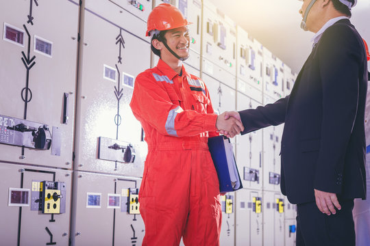 Electrical and instrument technician and businessman shake hand in front of electric system.