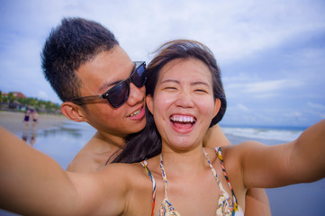 Fototapeta premium young happy and beautiful Asian Chinese couple taking selfie photo with mobile phone camera smiling joyful having fun on the beach