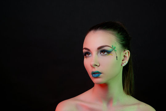 Glamorous brunette girl with fantasy make-up and coloured lights on the face on black background close-up