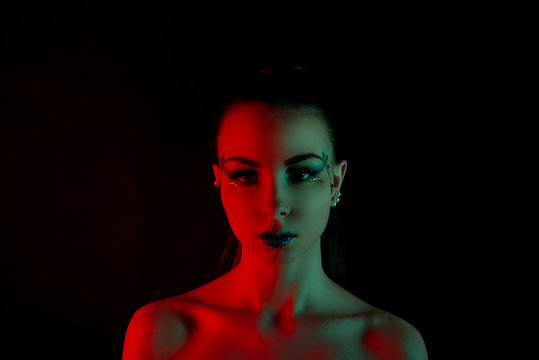Brunette girl with red and green illumination on the face against a black background closeup