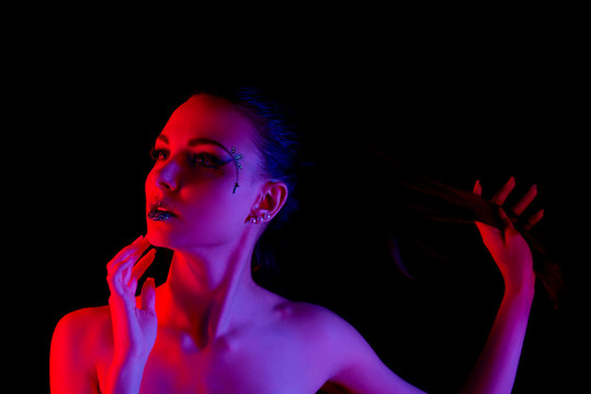Glamorous brunette girl holding her hair back in a red and purple lighting on a black background