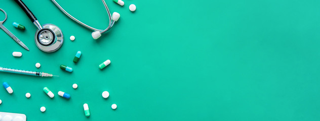 Pills and medical equiupments including stethoscope, syringe and scissors at border on green banner background, top view with copy space