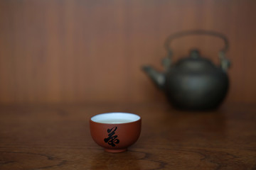 CHINESE TEA CUP WITH BLACL IRON KETTLE
Small ceramic Chinese tea cups are placed together with black iron kettle on the wood table in front of  wood wall.