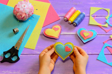 Child holds a felt heart gift in his hands. Child show a felt heart gift. Heart ornaments,...