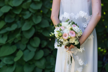 Bride holds in her hands wedding bouquet with pink and white roses on a greenery background