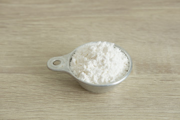 FLOUR IN MEASURING CUP
White flour in a measuring cup at the center on a wood table.