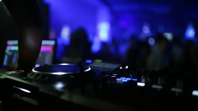 In the foreground is a sound mixer for the work of a DJ, and on the background of the back, dancing people.